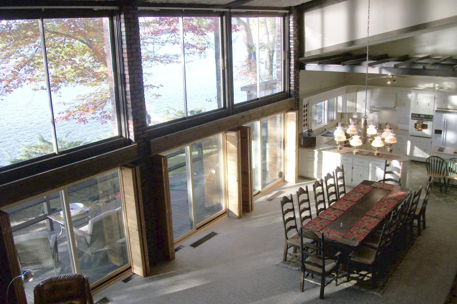 Great room features two stories of windows overlooking lake and has large dining table near kitchen